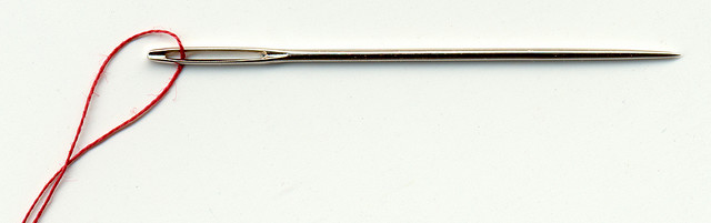 Needle with a red thread through the eye.